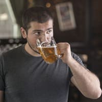 Homem jovem segurando um copo de bebida alcoólica em um bar, simbolizando o tema da dependência química e o consumo excessivo de álcool.
