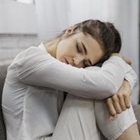 Mulher sentada abraçando os joelhos, com expressão de tristeza e olhar cabisbaixo, representando sintomas de depressão e isolamento emocional.